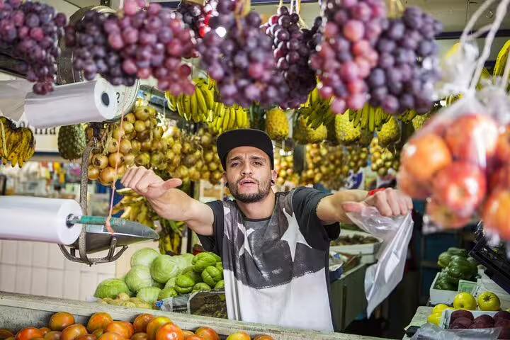 Fruit vendor showcasing a colorful array of grapes and tomatoes at a bustling San Jose market on the walking food tour.