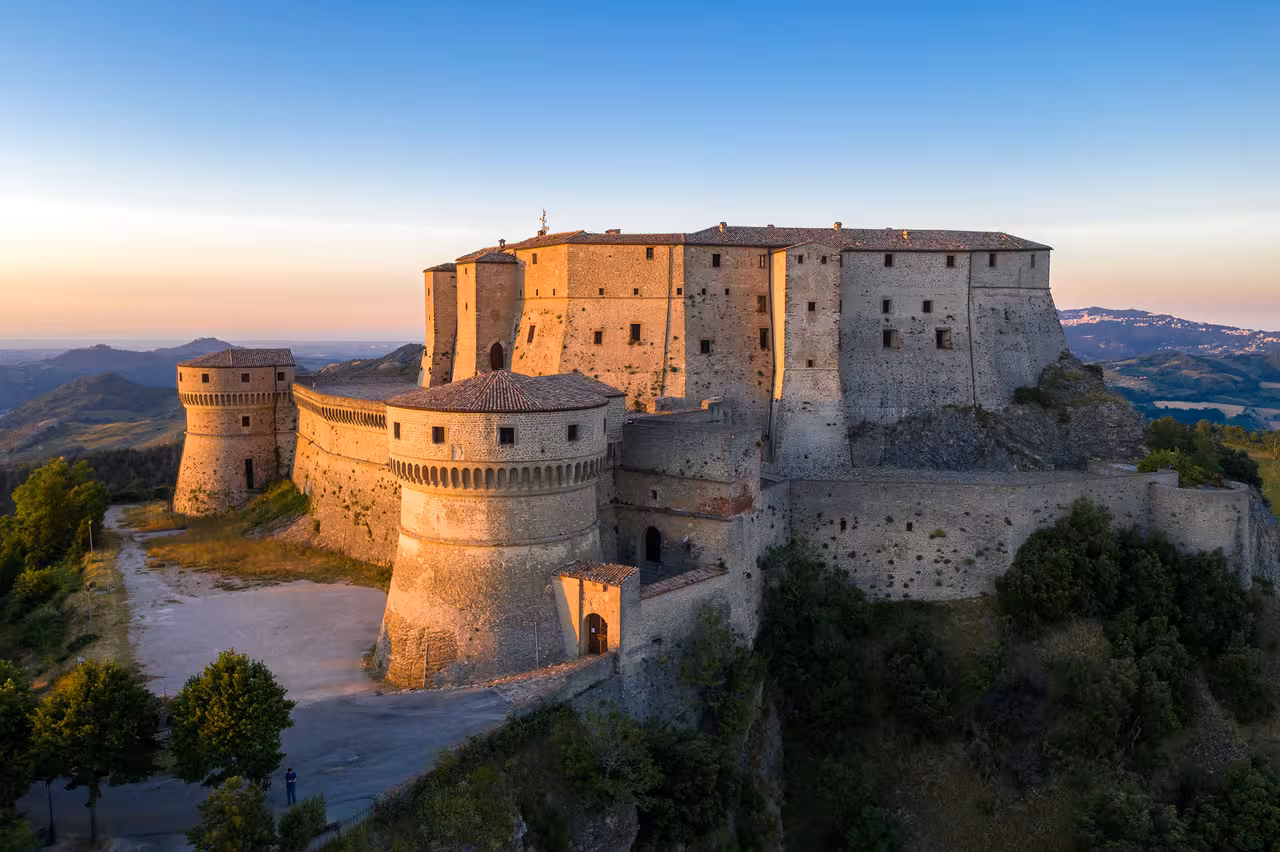 Sunset view of the San Leo fortress atop Montefeltro hills, highlighting medieval walls and panoramic Emilia-Romagna landscape