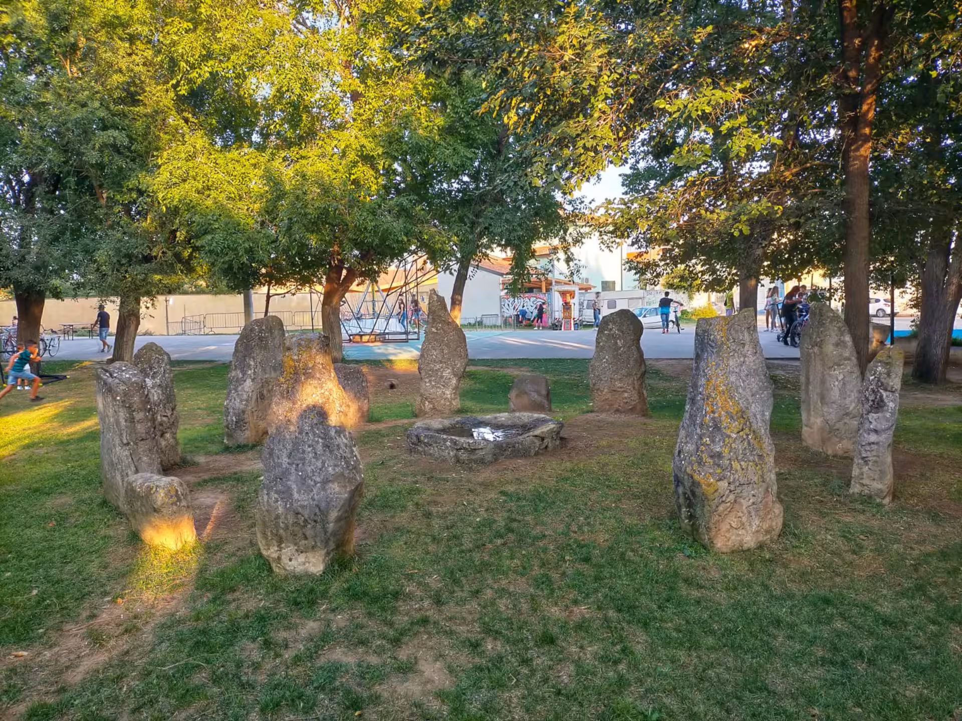 Ancient stone circle under trees in San Sperate village park, highlighting cultural heritage and history.
