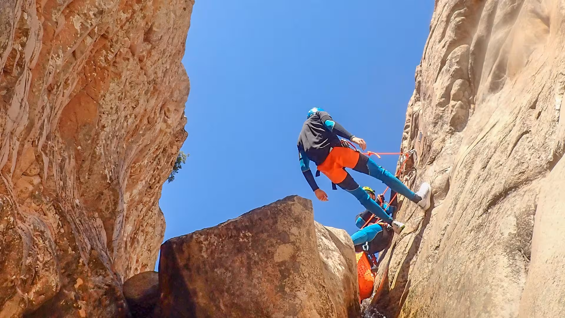 Adventurers canyoning in Rio Pitrisconi, San Teodoro, scaling rugged cliffs under clear blue skies.