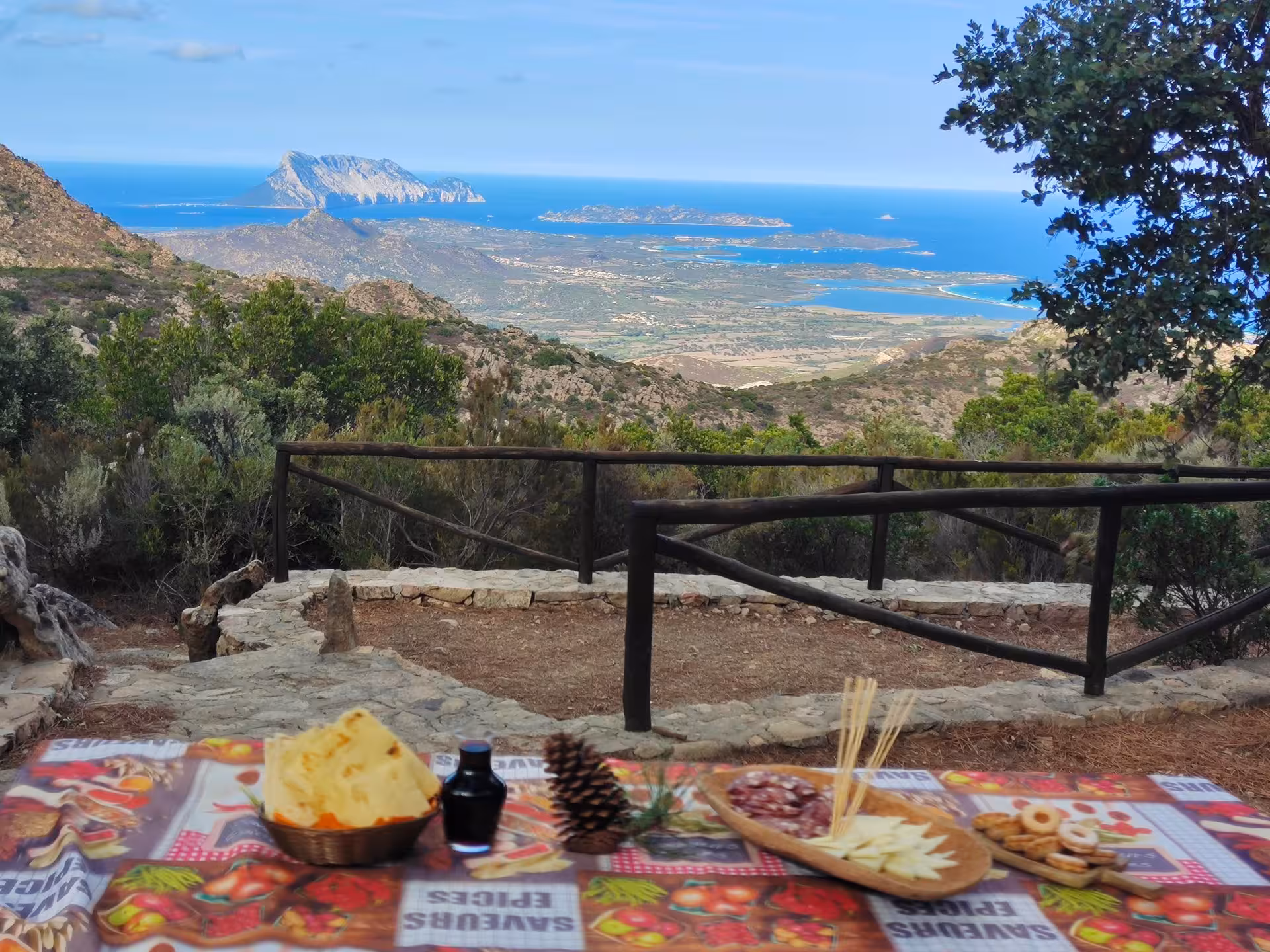Scenic view of Tavolara Island from San Teodoro with traditional Italian snacks on a table in the foreground.