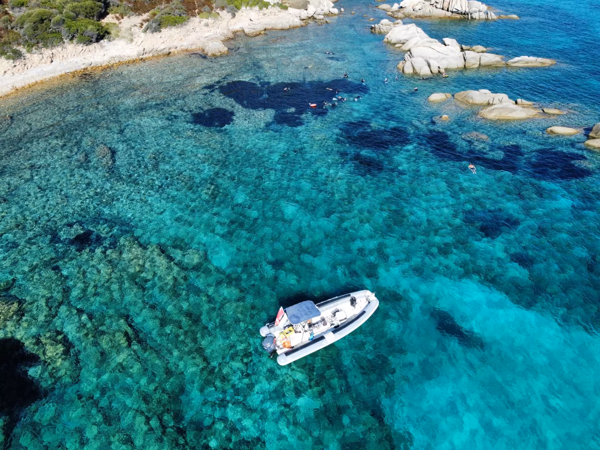 Aerial view of a boat and snorkelers exploring the vibrant turquoise waters near Molara Island in San Teodoro.