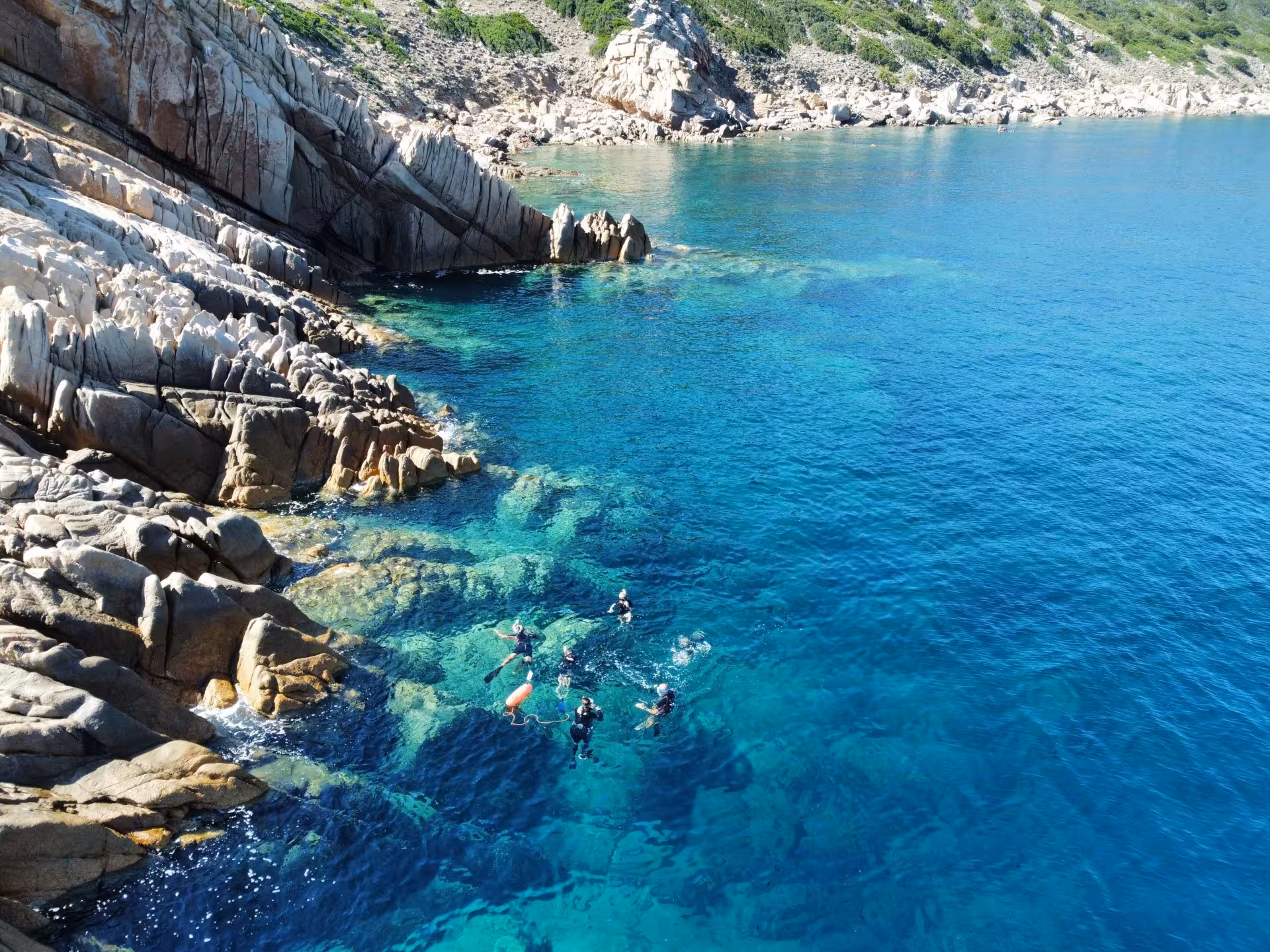 Snorkelers enjoying the crystal-clear blue waters and rocky coastline of Molara Island, San Teodoro.