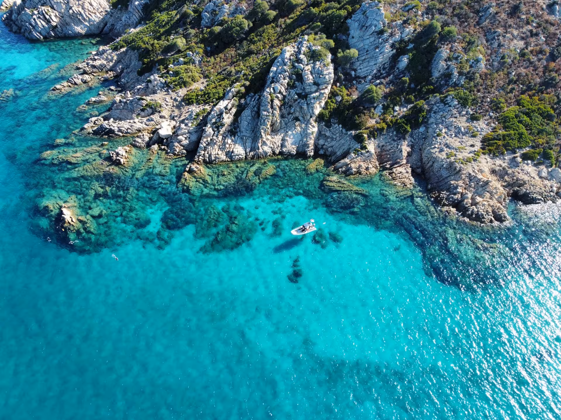 Pristine turquoise waters and rugged coastline of Molara, featuring a boat, ideal for snorkeling from San Teodoro.