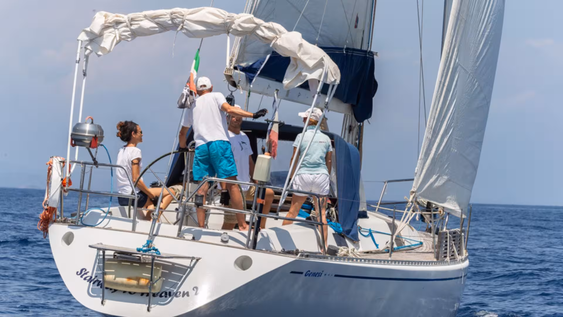 Group enjoying a sunny day on a sailing boat during the San Teodoro boat tour, with sails unfurled over blue waters.