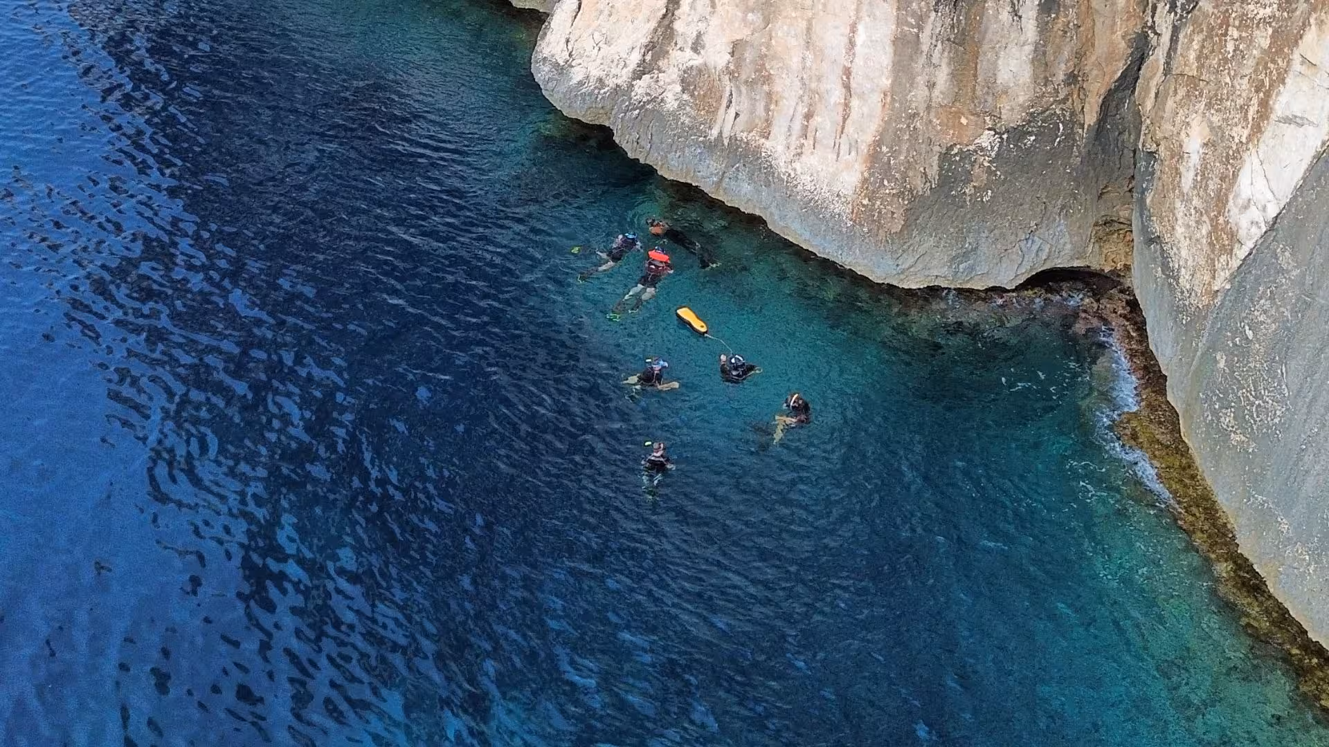 Snorkelers exploring the clear turquoise waters near rocky cliffs in Tavolara, offering a unique underwater experience.