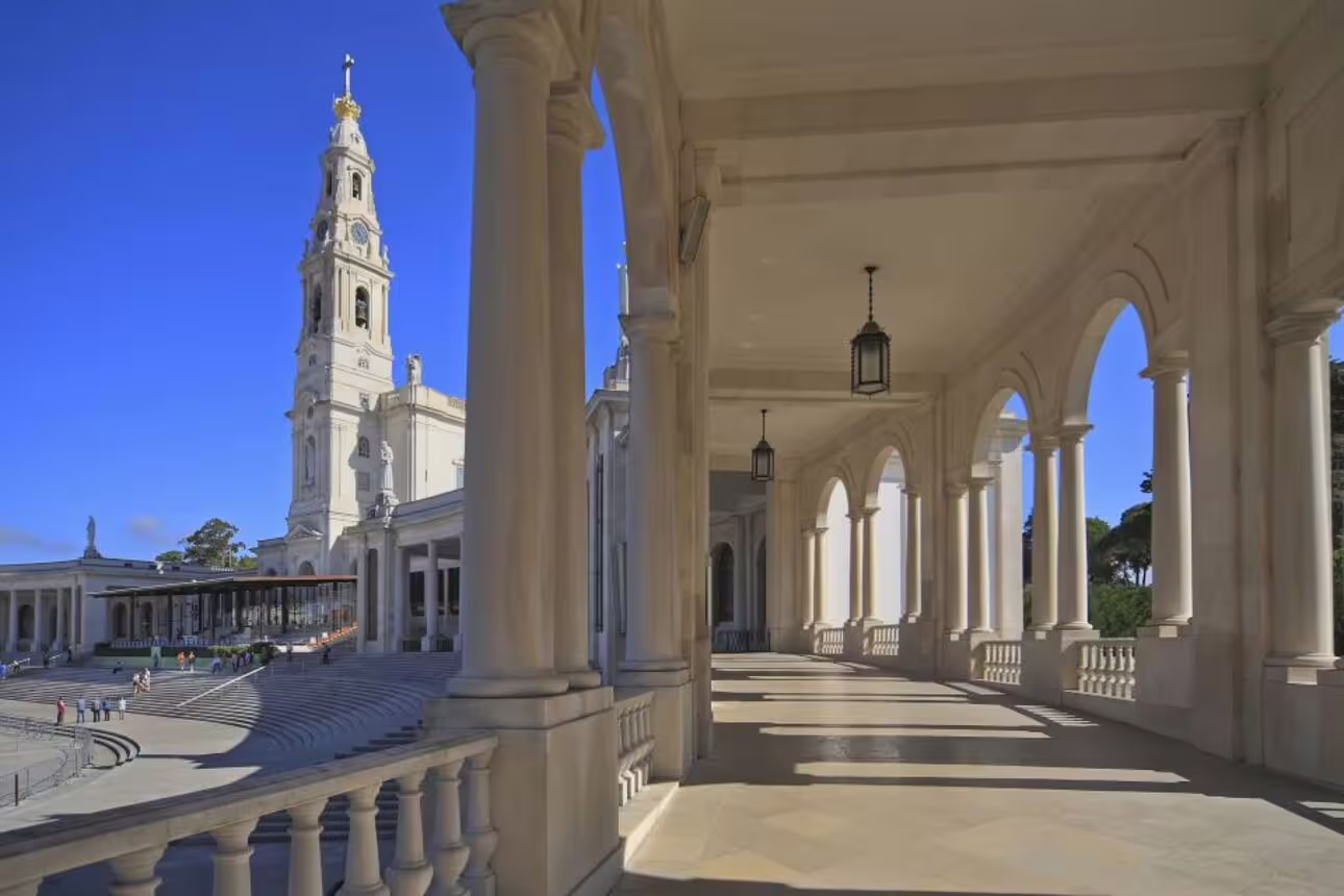 Elegant arched colonnade leading to the Sanctuary of Fátima under a clear blue sky, highlighting its grandeur.