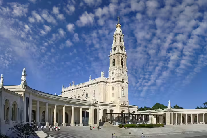Majestic view of the Sanctuary of Fátima under a vibrant blue sky, showcasing Portugal's rich cultural and spiritual heritage.