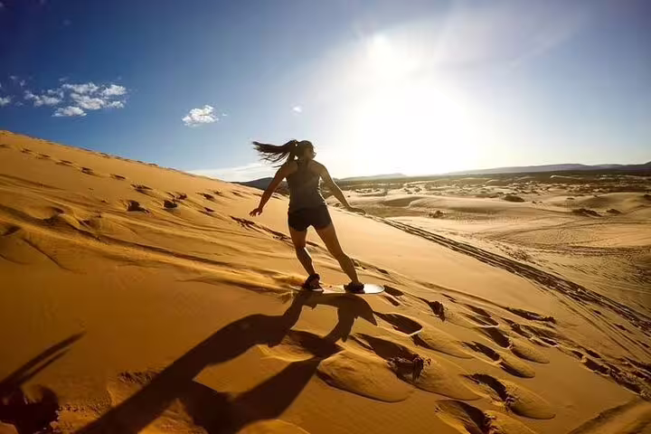 Experience thrilling sandboarding down golden dunes under a bright sun on a desert safari adventure.
