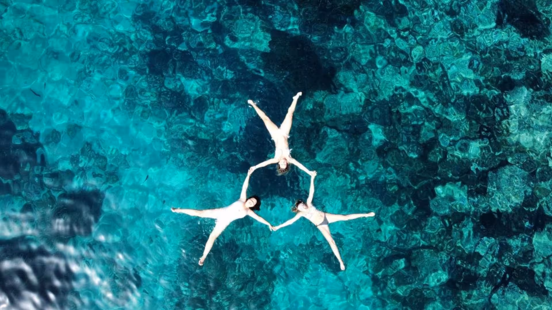 Three people forming a star shape while floating in pristine waters during a Sant'Antioco RIB tour, ideal for relaxation.