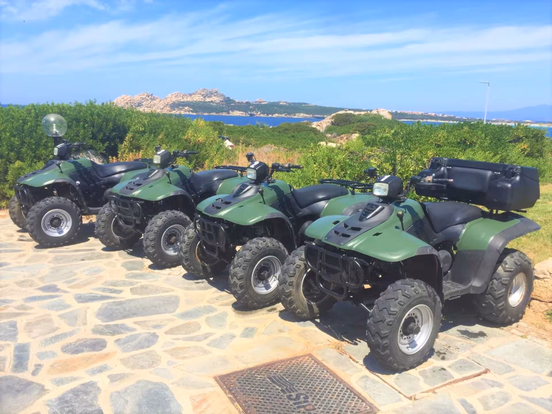 Four green ATVs parked on stone path overlooking scenic coastline, ideal for Santa Teresa di Gallura off-road tours.