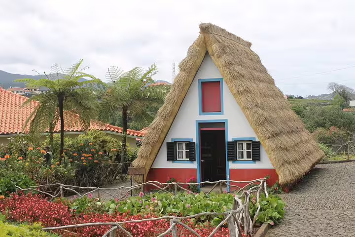 Traditional Santana A-frame house with thatched roof surrounded by vibrant flowers on the Northeast Madeira 4x4 tour.