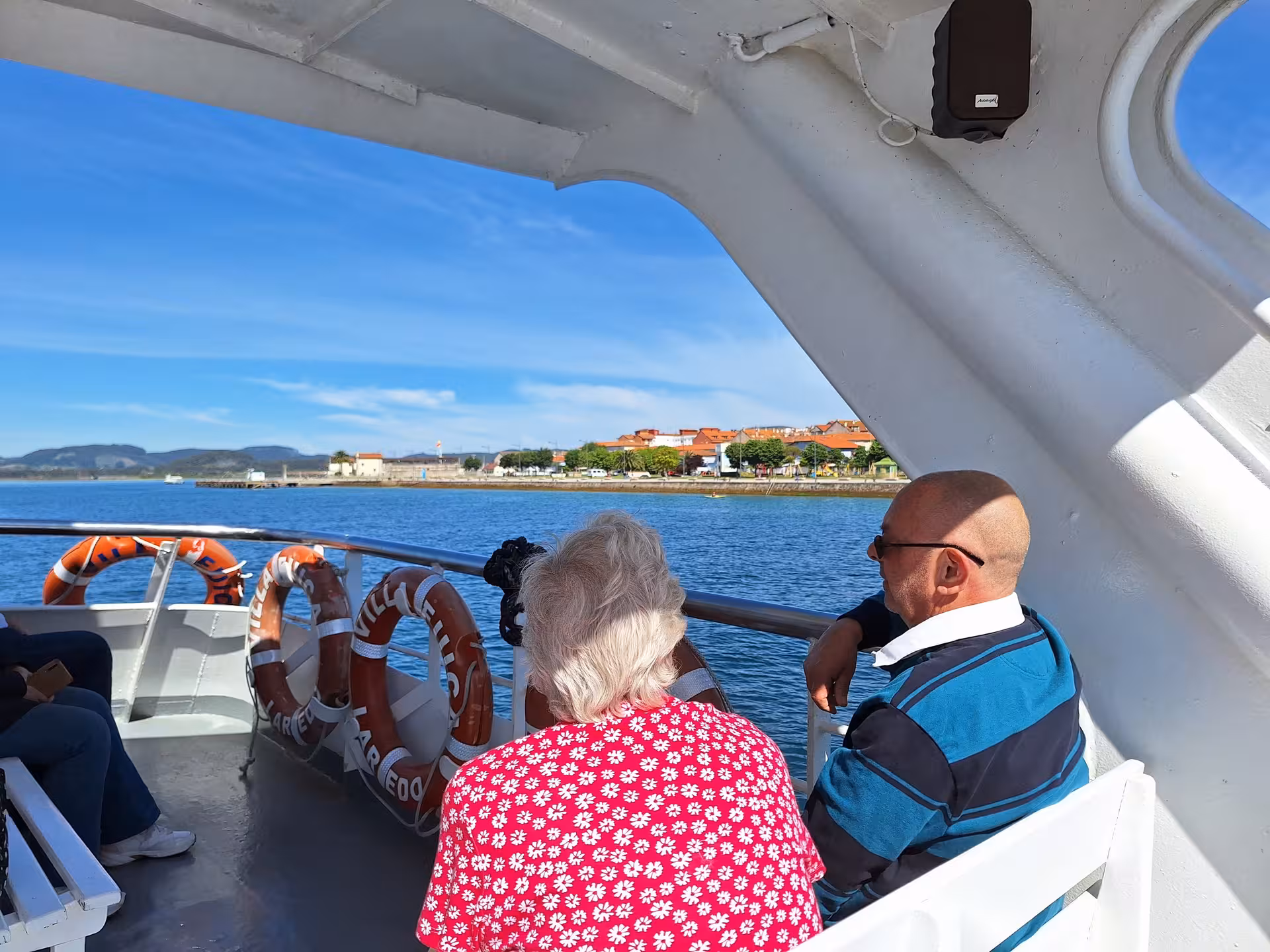 Passengers enjoy scenic views on a boat trip from Santander to Santoña under a clear blue sky.