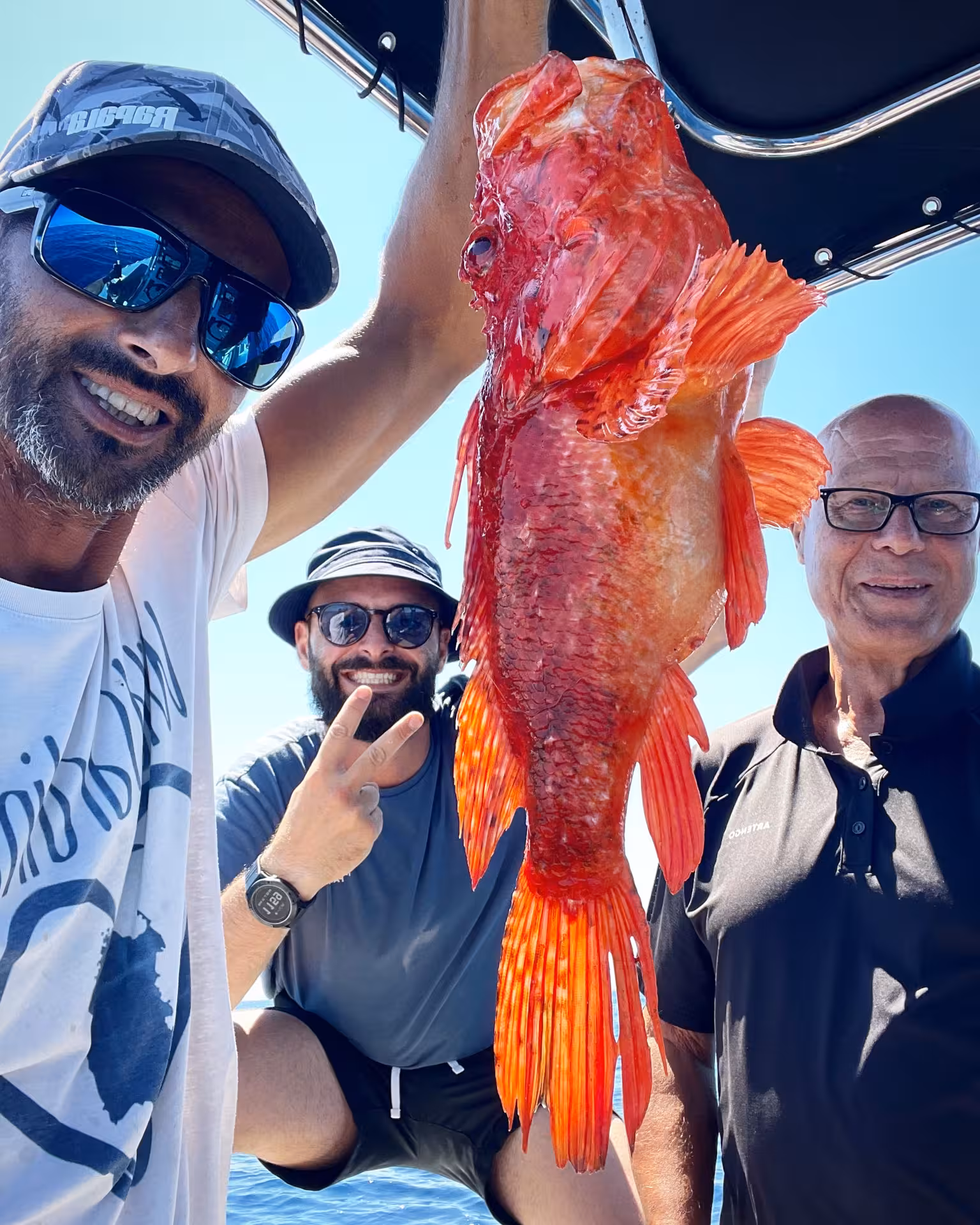 Group of friends display a vibrant red fish caught during a Sant'Antioco fishing charter adventure.