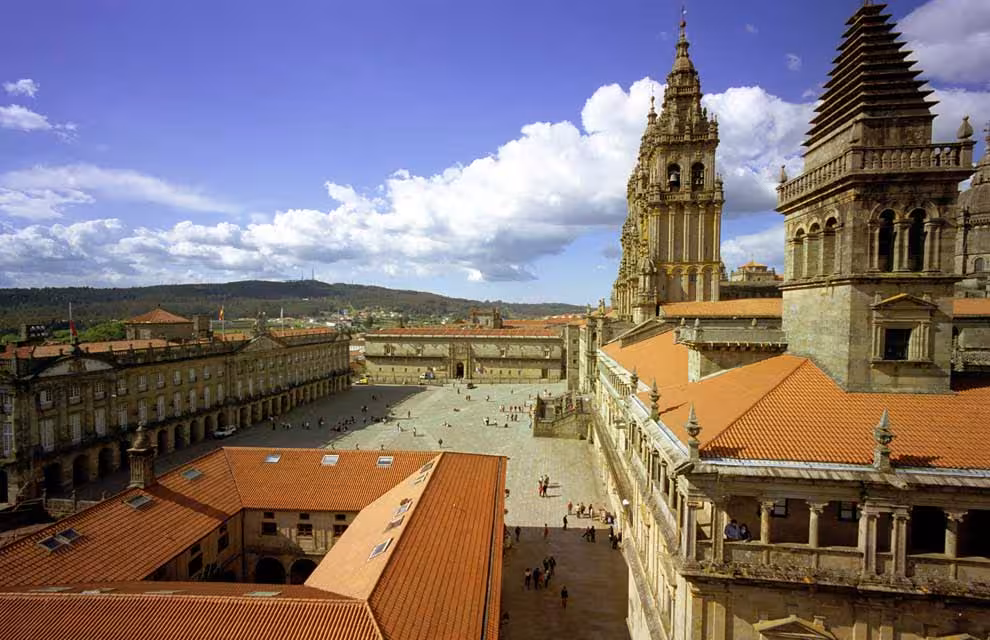 Aerial view of Santiago de Compostela Cathedral, showcasing its intricate towers and expansive plaza under a vibrant sky.
