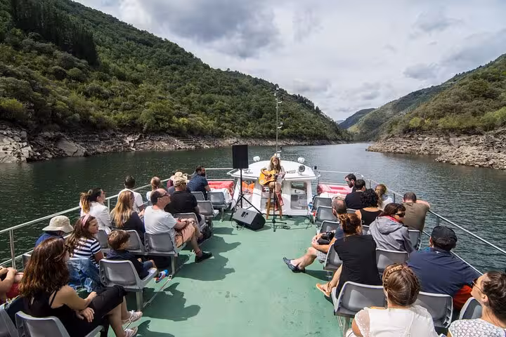 Tourists enjoy a live music performance aboard a scenic boat trip through the tranquil waters of Ribeira Sacra.