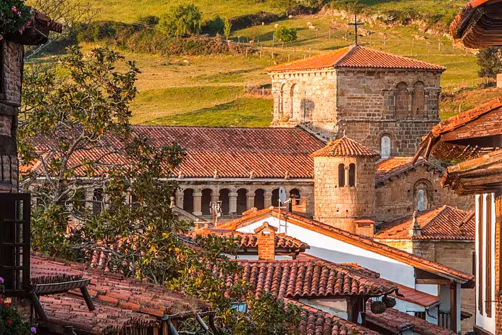 Historic church with red-tiled roofs surrounded by lush greenery in Santillana del Mar, showcasing medieval architecture.