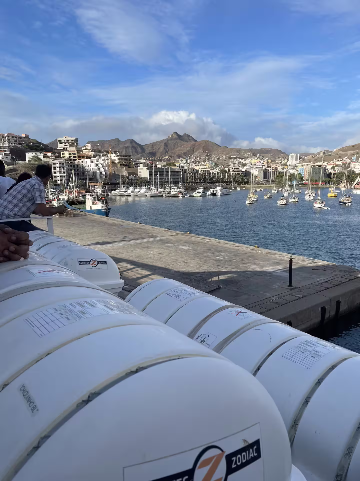 Scenic view of a bustling harbor in São Vicente with boats, mountains, and clear blue skies, perfect for a Santo Antão day trip.