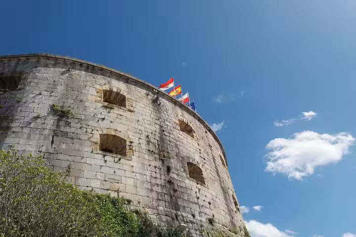 Historic stone fortress with colorful flags against a blue sky near Santoña, Spain.