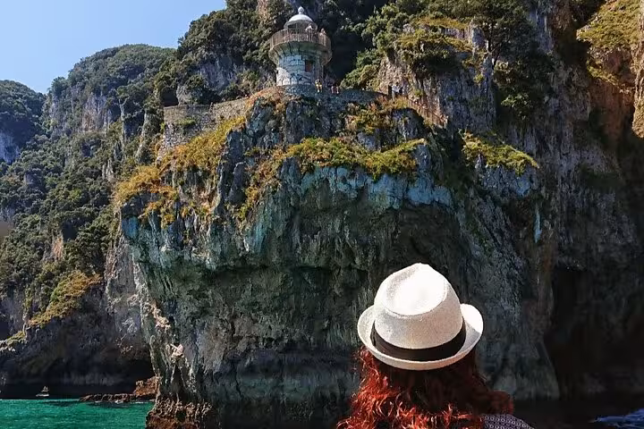 Visitor admires the rugged cliffs and historic lighthouse near Santoña during a boat excursion.