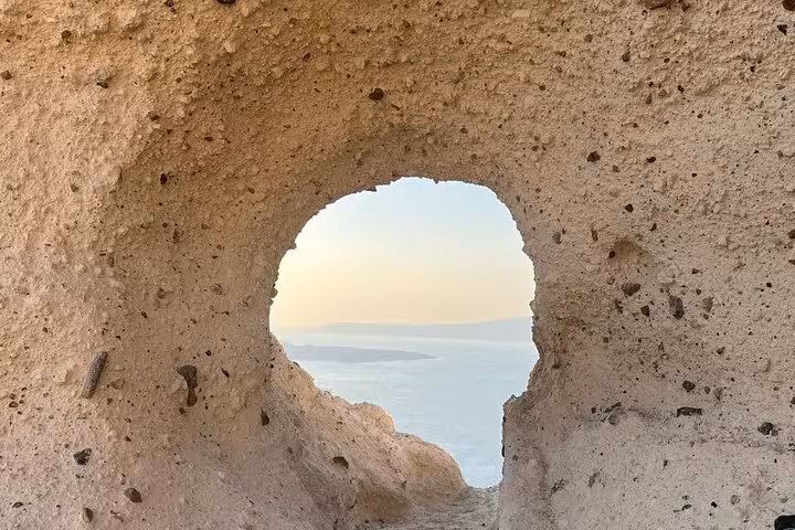Volcanic rock window framing the Santorini caldera sea view on a private island tour and cooking class day