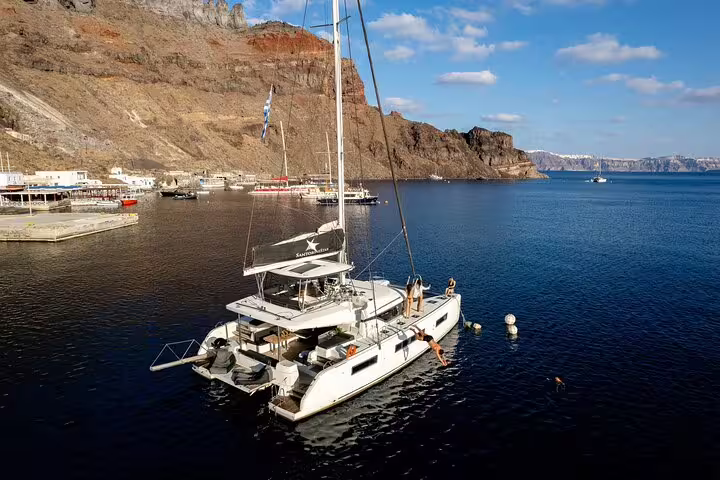 Catamaran anchored in Santorini's picturesque bay with passengers ready to explore the crystal-clear waters.