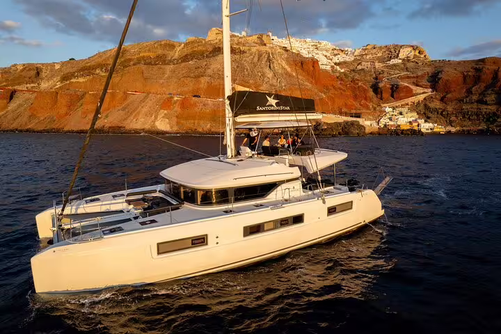 Luxurious catamaran sailing near Santorini's stunning cliffs during a half-day cruise with open bar and meal.