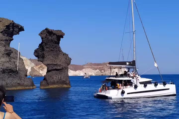 Catamaran cruising past striking rock formations on a Santorini half-day tour.