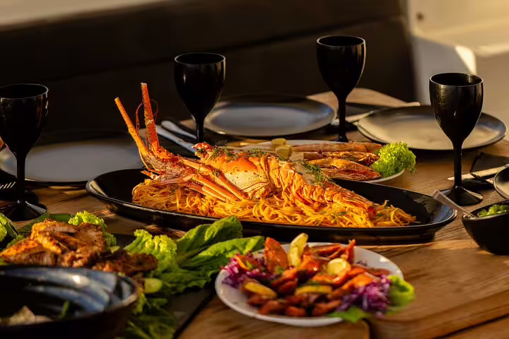 Gourmet seafood meal with lobster, pasta, and salads on a catamaran cruise in Santorini with open bar options.