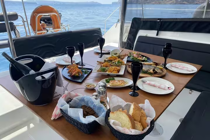 Gourmet seafood feast on a catamaran during a half-day cruise in Santorini, featuring wine and stunning sea views.