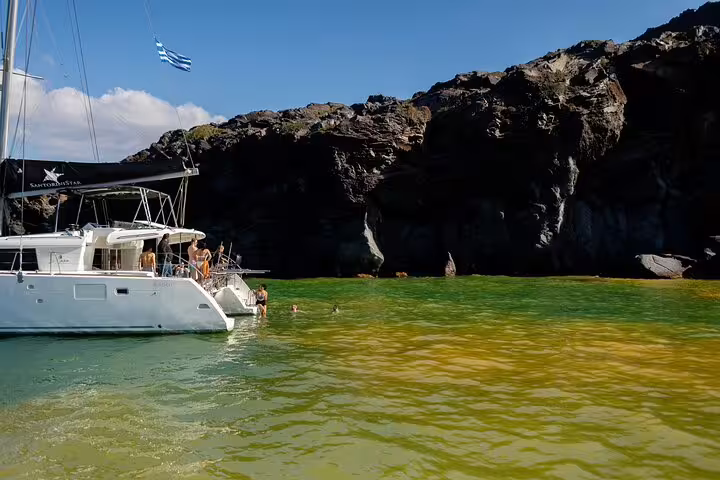 Catamaran anchored near volcanic cliffs in Santorini, offering guests a chance to swim in clear waters.