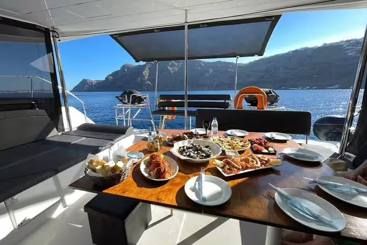 Elegant dining setup on a catamaran with gourmet seafood and stunning sea views in Santorini.