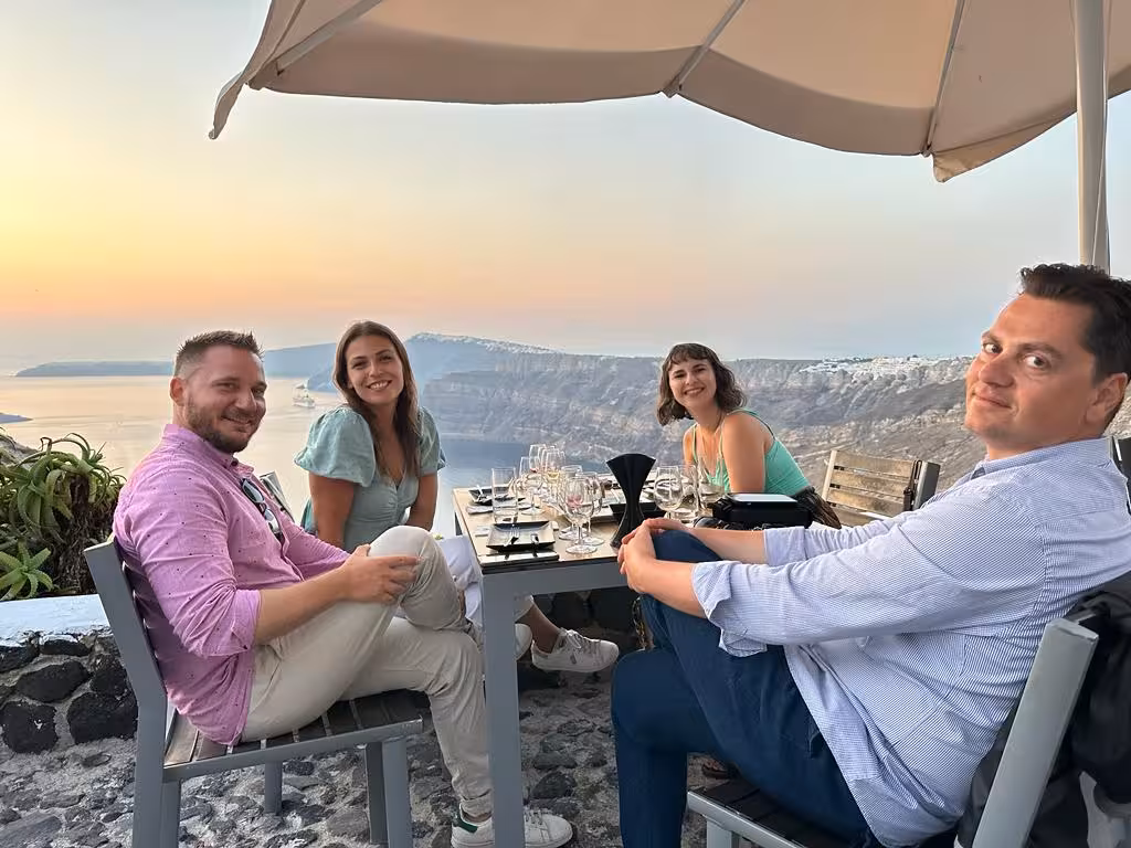 Friends dining at a cliffside restaurant with caldera sunset views on a Santorini private shore excursion tour