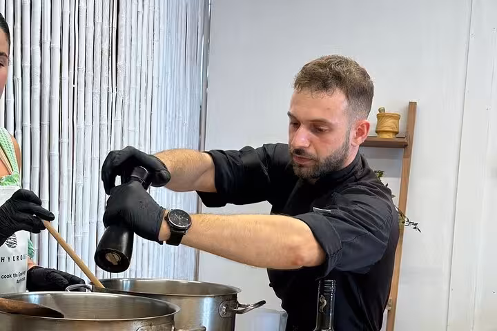 Chef seasoning a simmering pot in a Santorini private cooking class, part of an island tour experience