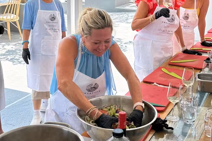 Traveler mixes fresh vegetables in a bowl during a Santorini private cooking class, hands-on Greek cuisine experience