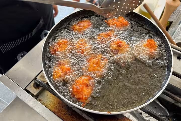 Greek tomato fritters frying in pan during Santorini cooking class, a tasty step before winery tastings