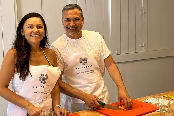 Smiling couple prepping ingredients in Santorini cooking class, honeymoon experience paired with two winery visits
