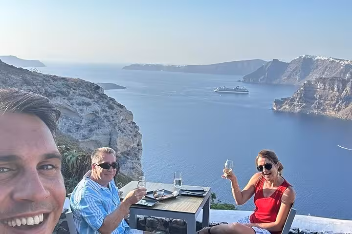 Couple toasting wine on Santorini caldera terrace, part of Thera 8-hour island tour with lunch and wine tasting