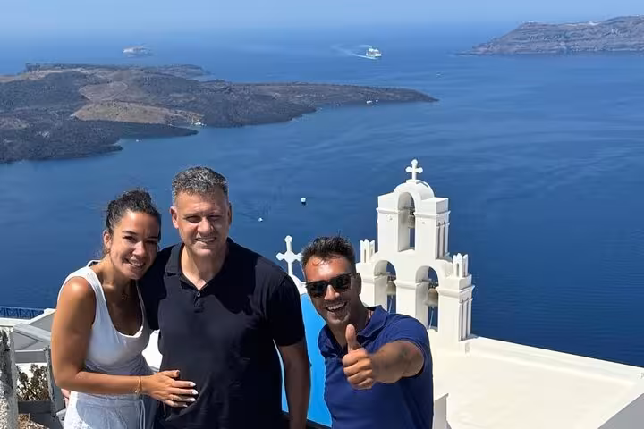 Happy travelers with Santorini caldera and white church in Oia on one-day cruise ship island tour