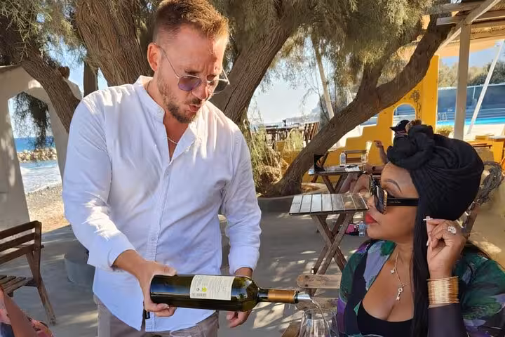 Private Santorini day trip from Crete with beachside wine tasting and local guide pouring Greek wine