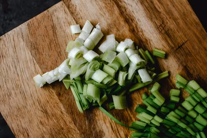 Chopped spring onions on a wooden board, prep step for hands-on Greek cooking class with caldera views