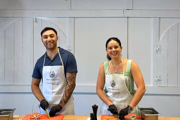 Smiling couple prepping ingredients in aprons at Santorini honeymoon cooking class before visiting two wineries