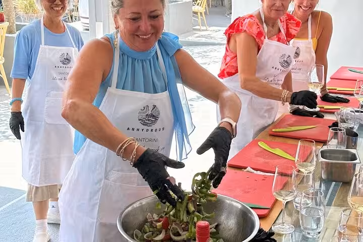 Guests toss Greek salad in Santorini honeymoon cooking class, enjoying wine tasting at two wineries