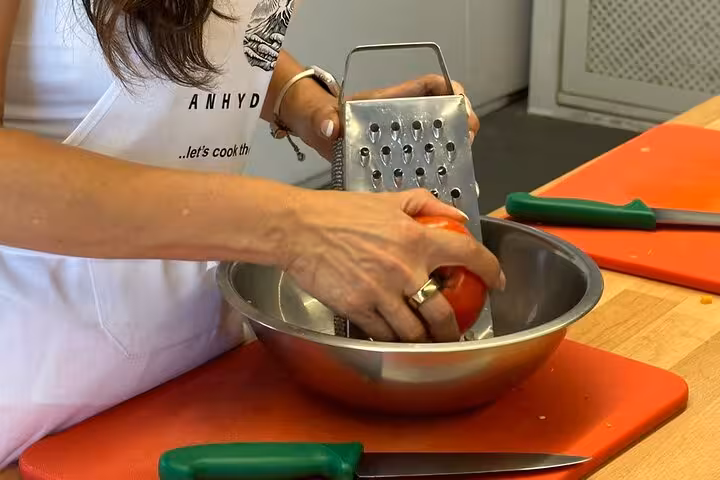 Hands grating fresh tomato in bowl during Santorini honeymoon cooking class before winery tasting tour