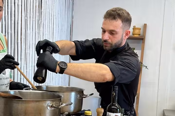 Santorini chef seasoning pots during honeymoon cooking class, paired with two local winery tastings