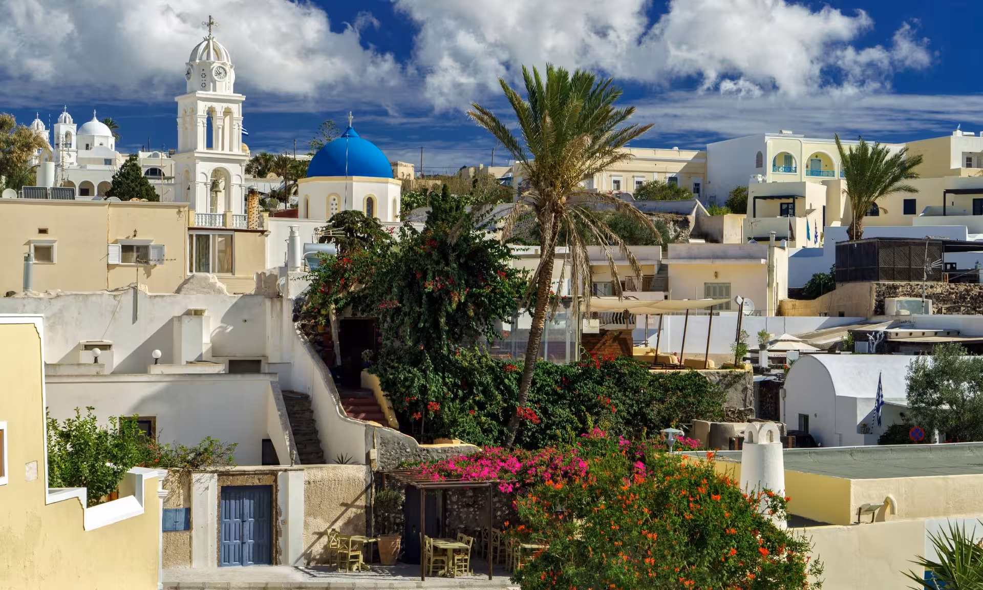 Panoramic Santorini tour view of Fira with blue-domed church, whitewashed houses, and palm trees