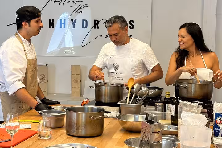 Chef and guests cook together at a Santorini private cooking class, learning Greek dishes in a modern kitchen