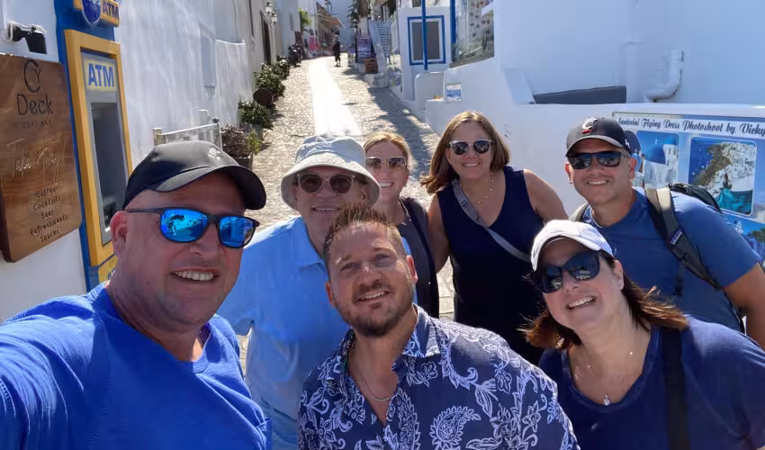 Happy travelers with local guide in a whitewashed Santorini lane on a private highlights shore excursion