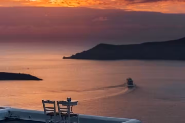 Romantic Santorini sunset terrace with sea view and passing boat, ideal for private honeymoon wine tour