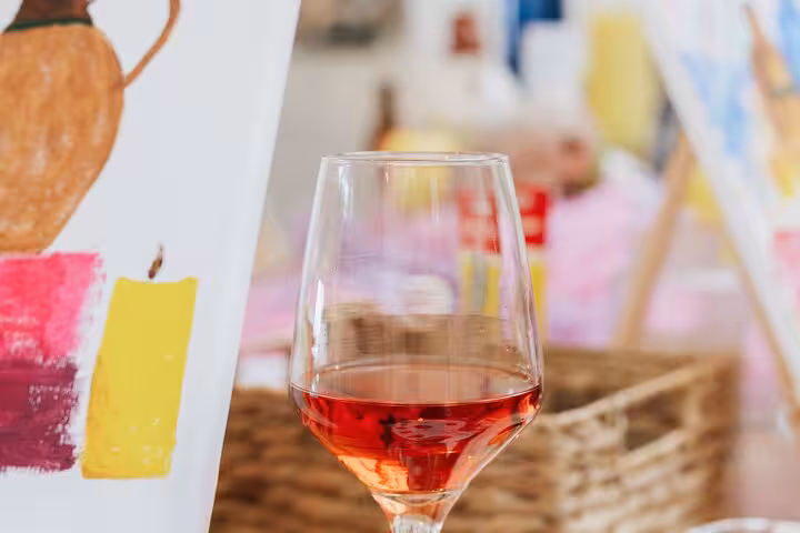 Glass of Santorini rosé beside a colorful canvas, capturing the Wine and Paint experience in Greece
